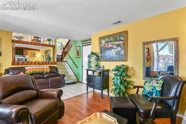 living room with visible vents, a textured ceiling, wood finished floors, and stairs