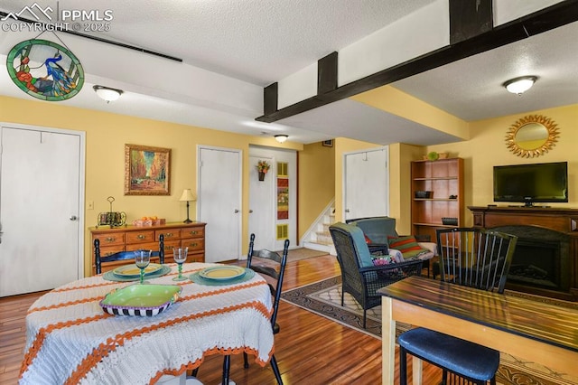 dining area featuring a fireplace, a textured ceiling, stairs, and wood finished floors