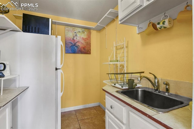 kitchen with light countertops, light tile patterned floors, freestanding refrigerator, white cabinets, and a sink