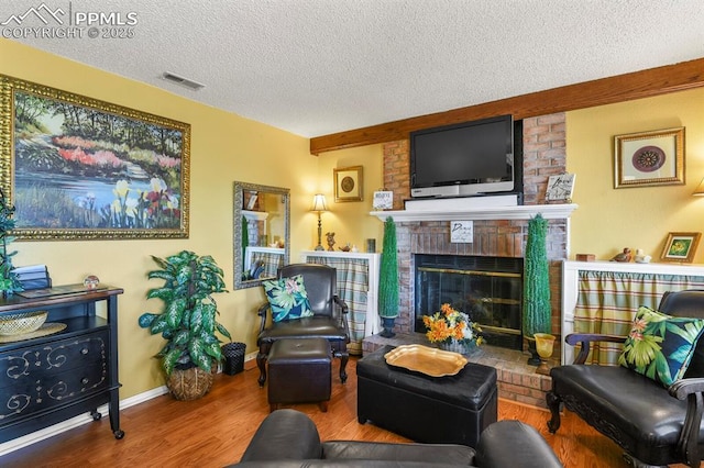 living area featuring visible vents, a brick fireplace, baseboards, wood finished floors, and a textured ceiling