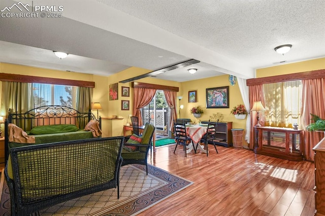 bedroom featuring access to outside, wood finished floors, beamed ceiling, and a textured ceiling