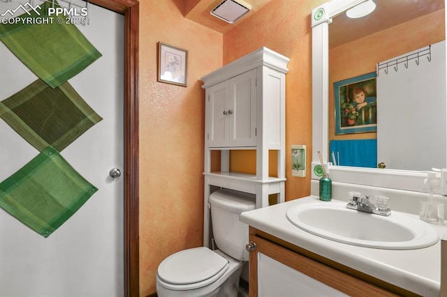 bathroom with vanity, toilet, a textured wall, and visible vents