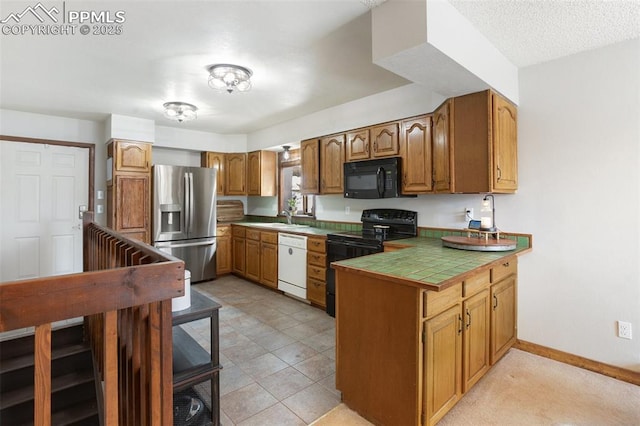 kitchen with a peninsula, baseboards, a sink, black appliances, and brown cabinetry