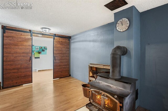 interior space with a barn door, wood finished floors, a wood stove, and a textured ceiling