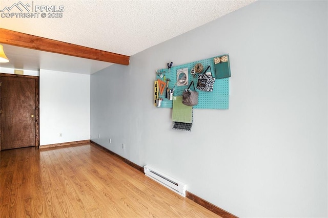 empty room with beamed ceiling, wood finished floors, a baseboard heating unit, and a textured ceiling