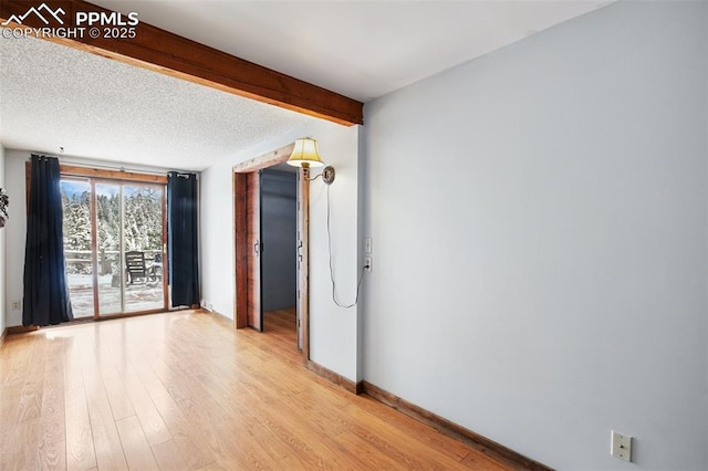 empty room featuring baseboards, a textured ceiling, beamed ceiling, and light wood-type flooring