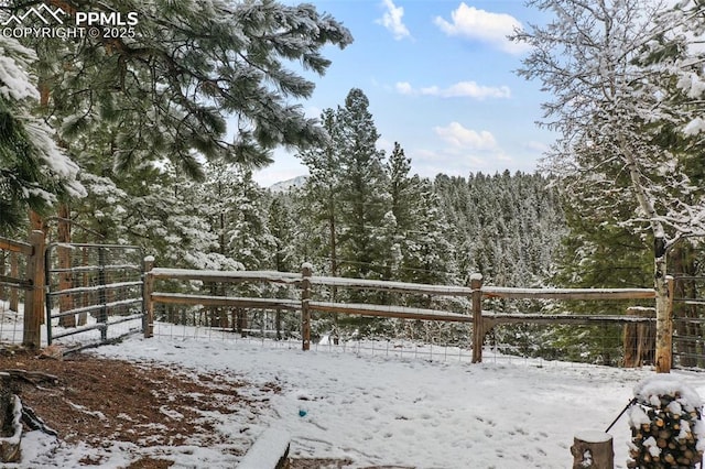 yard layered in snow featuring a wooded view and fence