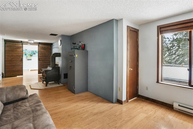 living room featuring a wood stove, baseboards, a textured ceiling, light wood-style floors, and baseboard heating