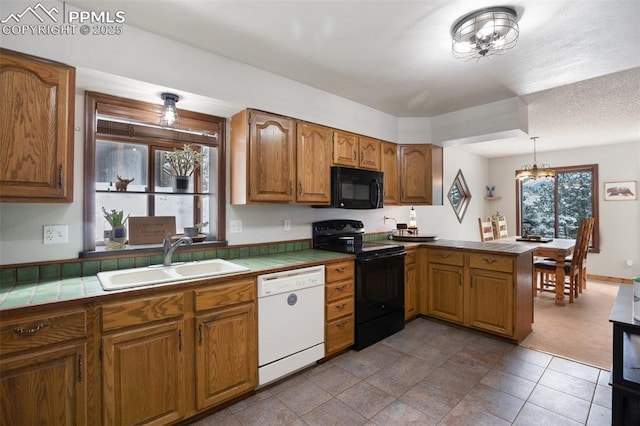 kitchen with a sink, tile countertops, a peninsula, black appliances, and brown cabinetry