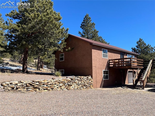 view of side of home with a wooden deck, stairs, and stucco siding