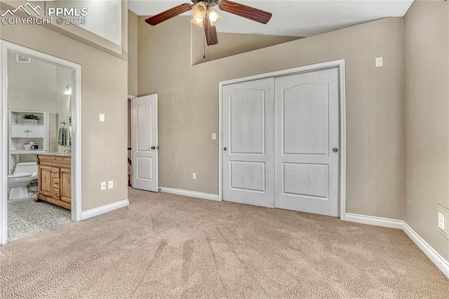 unfurnished bedroom featuring light carpet, high vaulted ceiling, ensuite bathroom, a closet, and baseboards