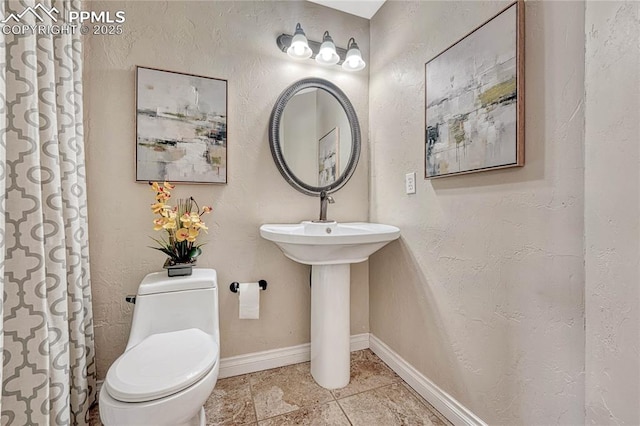 bathroom featuring baseboards, toilet, and a textured wall