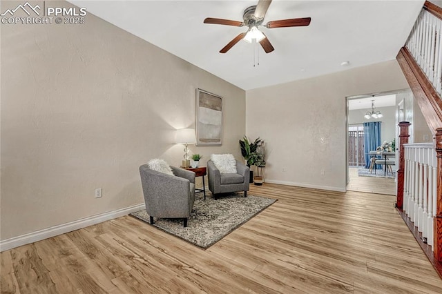 sitting room with ceiling fan with notable chandelier, baseboards, and wood finished floors