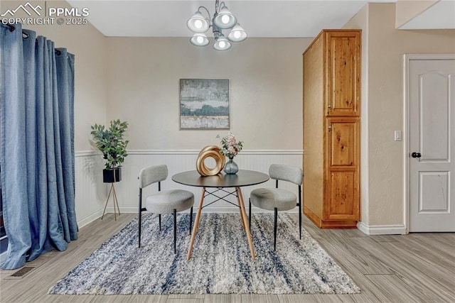 dining area with a notable chandelier, a wainscoted wall, and wood finished floors