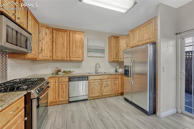 kitchen with light stone counters, stainless steel appliances, light wood-type flooring, and a sink