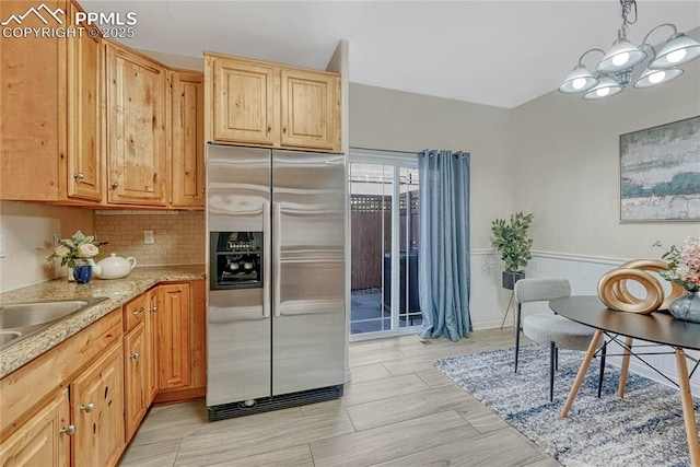 kitchen featuring light stone counters, a wainscoted wall, hanging light fixtures, stainless steel fridge, and backsplash