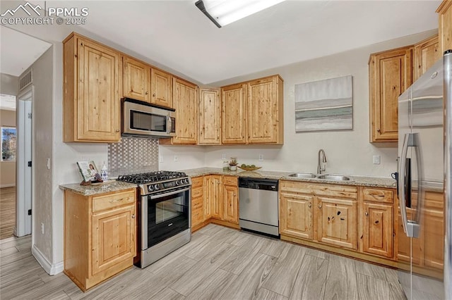 kitchen featuring light wood-style flooring, a sink, light stone counters, backsplash, and stainless steel appliances