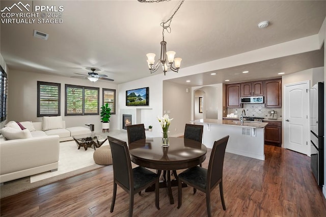 dining room featuring visible vents, arched walkways, a glass covered fireplace, and dark wood-style flooring