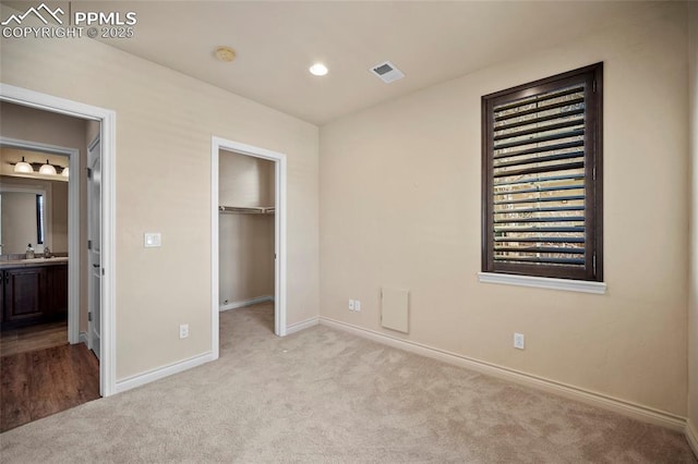 unfurnished bedroom featuring baseboards, visible vents, carpet floors, recessed lighting, and a walk in closet