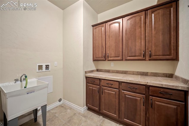 washroom featuring a sink, baseboards, cabinet space, and hookup for a washing machine