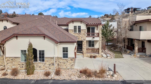 view of front of property featuring stucco siding, stone siding, a balcony, and a shingled roof