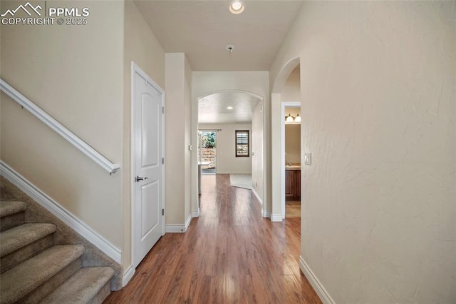 hallway with wood finished floors, baseboards, recessed lighting, arched walkways, and stairs