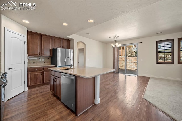 kitchen with a center island with sink, decorative backsplash, arched walkways, stainless steel appliances, and dark wood-style flooring