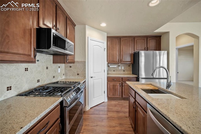 kitchen with wood finished floors, light stone countertops, stainless steel appliances, and a sink