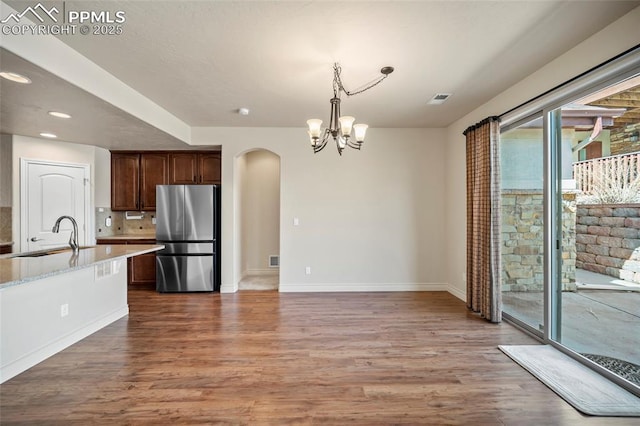 kitchen featuring arched walkways, wood finished floors, freestanding refrigerator, and a sink