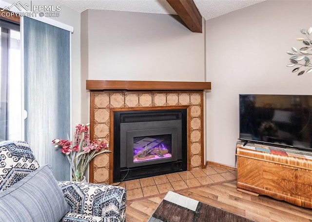 living room featuring beamed ceiling, a fireplace with flush hearth, a textured ceiling, and wood finished floors