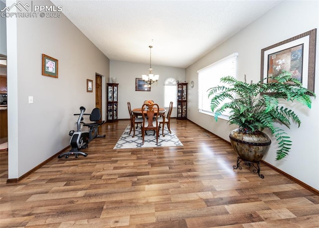 dining space with baseboards, a textured ceiling, a chandelier, and light wood finished floors