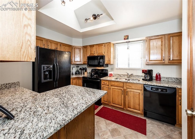 kitchen featuring light stone counters, a sink, decorative backsplash, black appliances, and brown cabinets