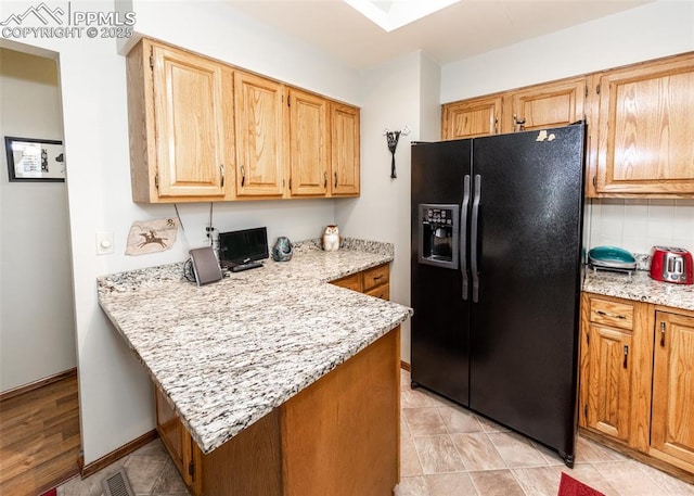 kitchen featuring light stone counters, visible vents, a peninsula, black fridge with ice dispenser, and backsplash