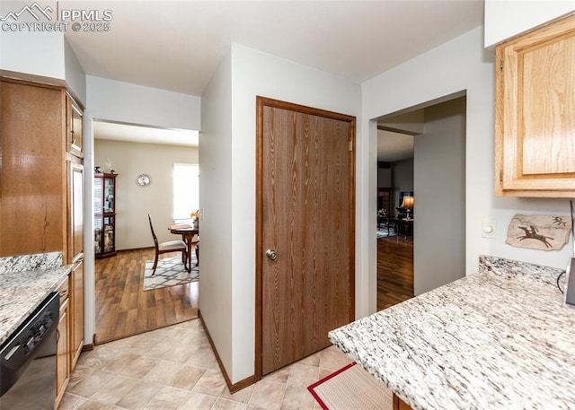 kitchen featuring light brown cabinetry, light stone counters, baseboards, and black dishwasher