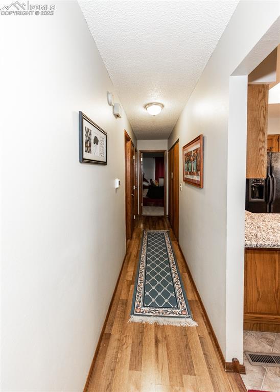 hallway featuring light wood-style flooring, baseboards, visible vents, and a textured ceiling