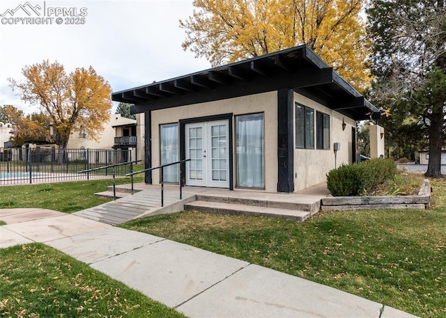 rear view of house with a lawn, french doors, fence, and stucco siding