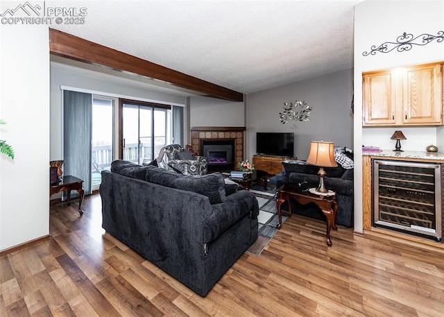 living area with beam ceiling, wine cooler, light wood-style flooring, and a textured ceiling