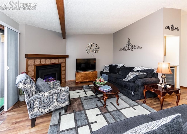 living room featuring a stone fireplace, a textured ceiling, lofted ceiling, and wood finished floors