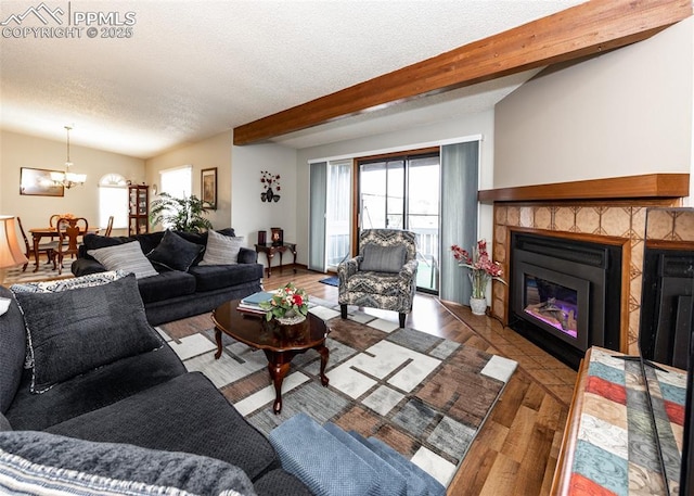 living area featuring beam ceiling, a notable chandelier, a textured ceiling, a glass covered fireplace, and wood finished floors