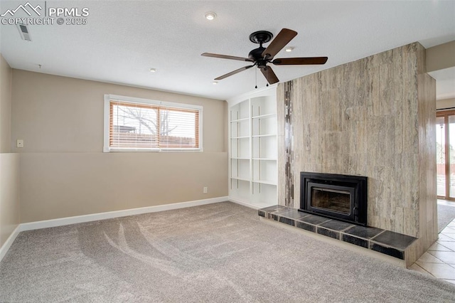 unfurnished living room featuring baseboards, a tiled fireplace, carpet flooring, a textured ceiling, and a ceiling fan