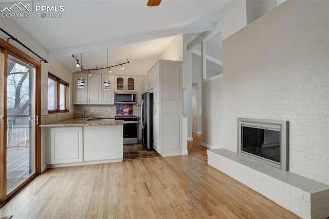 kitchen featuring a glass covered fireplace, a peninsula, appliances with stainless steel finishes, decorative backsplash, and vaulted ceiling