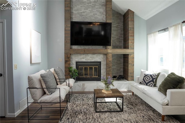 living room featuring wood finished floors, baseboards, visible vents, lofted ceiling, and a fireplace