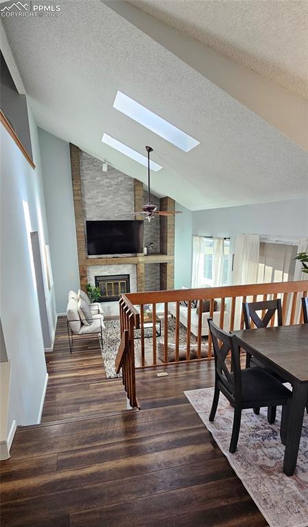 dining space featuring a large fireplace, a textured ceiling, wood finished floors, and vaulted ceiling with skylight