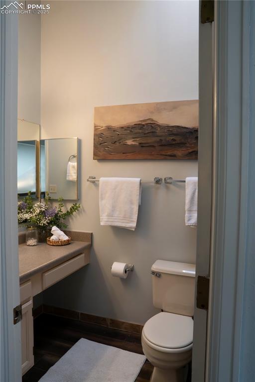 half bathroom featuring vanity, toilet, wood finished floors, and baseboards