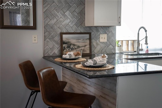 kitchen featuring a breakfast bar, white cabinets, backsplash, and a sink