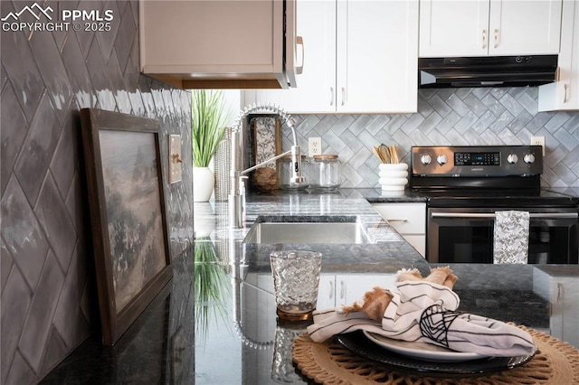 kitchen featuring under cabinet range hood, stainless steel electric range oven, dark stone countertops, and white cabinetry