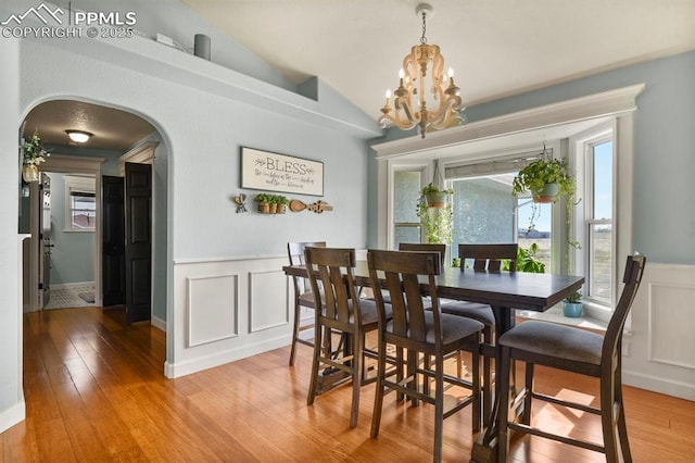 dining space featuring arched walkways, a wainscoted wall, light wood-style flooring, and vaulted ceiling