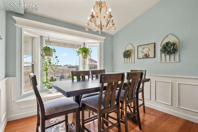 dining area featuring wood finished floors, wainscoting, a decorative wall, lofted ceiling, and a chandelier