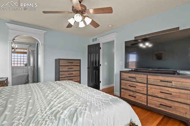 bedroom featuring a ceiling fan, visible vents, wood finished floors, arched walkways, and connected bathroom