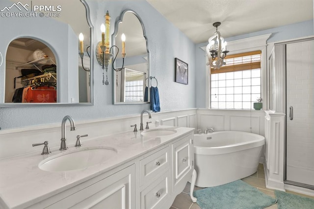 full bath with tile patterned floors, a wainscoted wall, an inviting chandelier, and a sink